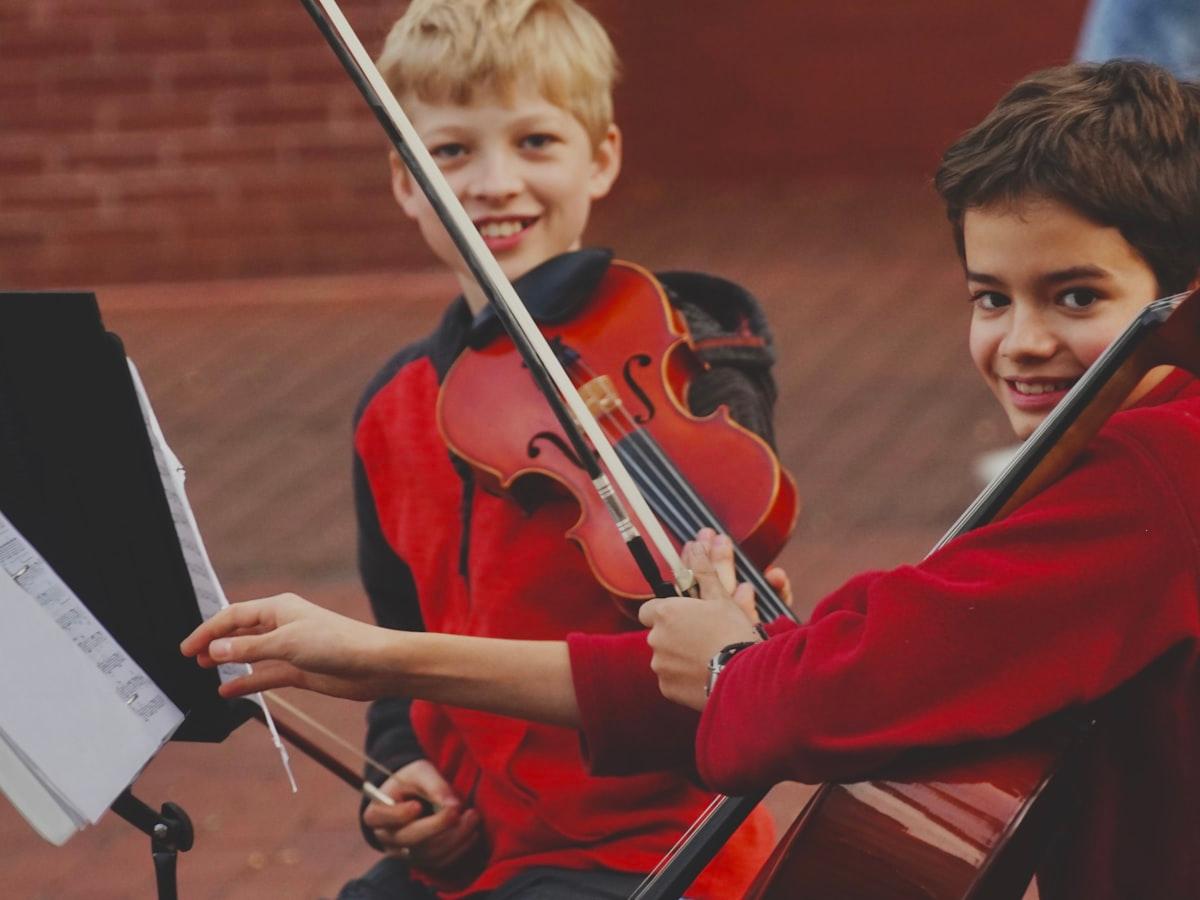 Two children playing string instruments at a music stand